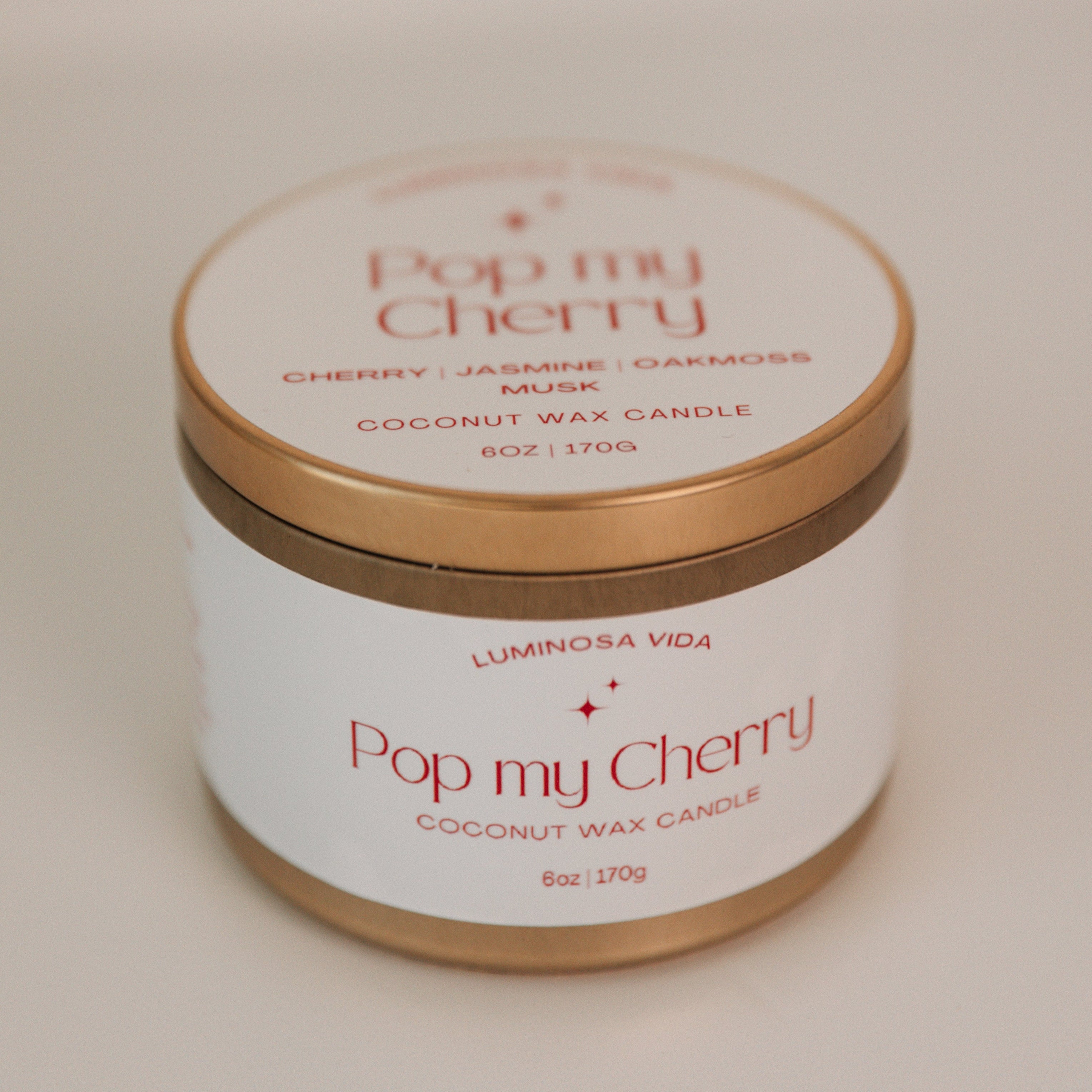 Playful candle labeled 'Pop My Cherry,' featuring a vibrant red wax in a sleek container, styled with fresh cherries and scattered petals for a fun and seductive vibe