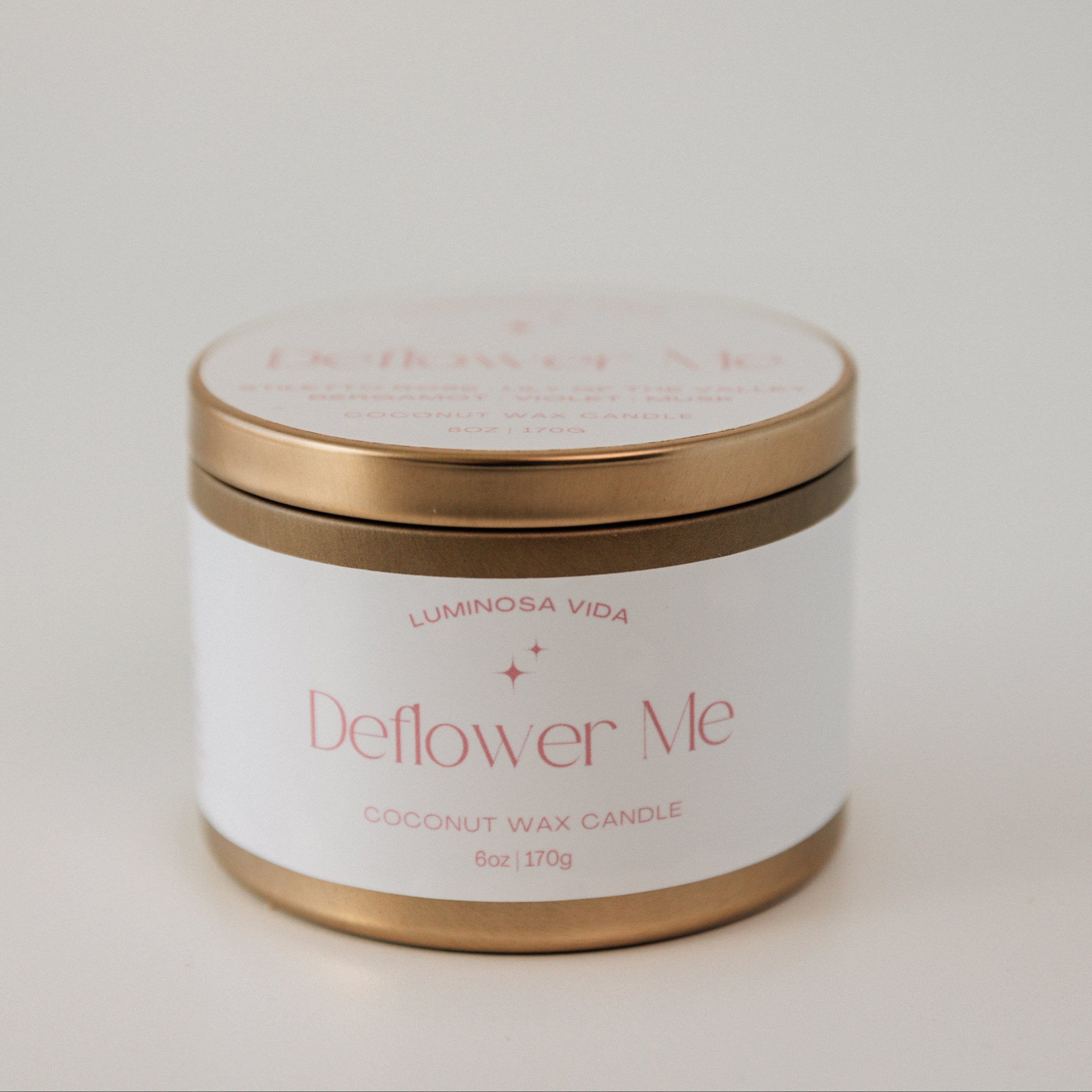 Elegant candle labeled 'Deflower Me,' featuring a soft blush pink wax in a chic container, surrounded by delicate petals of roses and peonies. The romantic setup exudes a playful yet seductive charm."