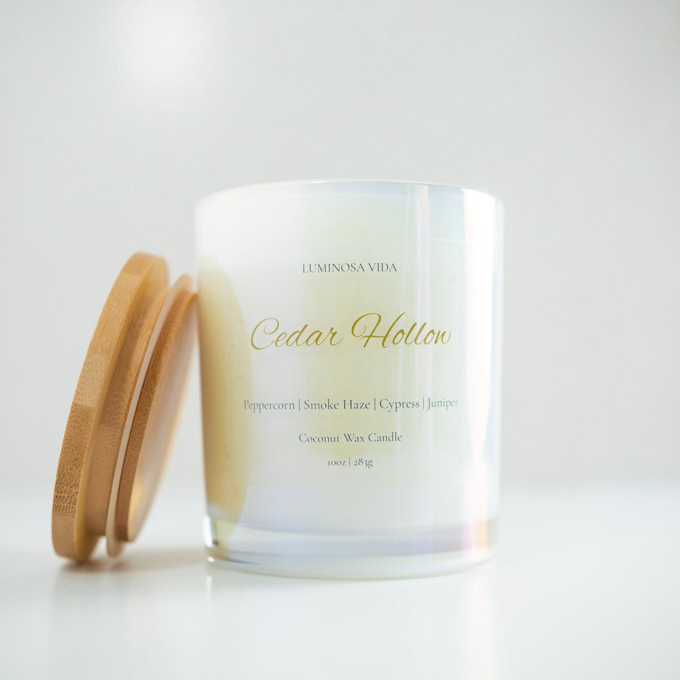 “Luminosa Vida Cedar Hollow candle in an iridescent glass jar with a wooden lid. Handcrafted coconut wax candle made in Austin, Texas with notes of peppercorn, smoke haze, cypress, and juniper — a warm and earthy winter scent.”