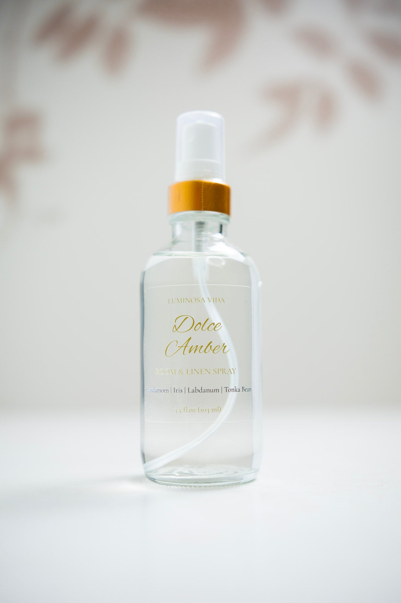 “Dolce Amber Room + Linen Spray by Luminosa Vida displayed on a white surface with a soft neutral background. A clear glass bottle with a gold cap and elegant label featuring scent notes of Cardamom, Iris, Labdanum, and Tonka Bean — a luxury, non-toxic home fragrance handcrafted in Austin, Texas.”