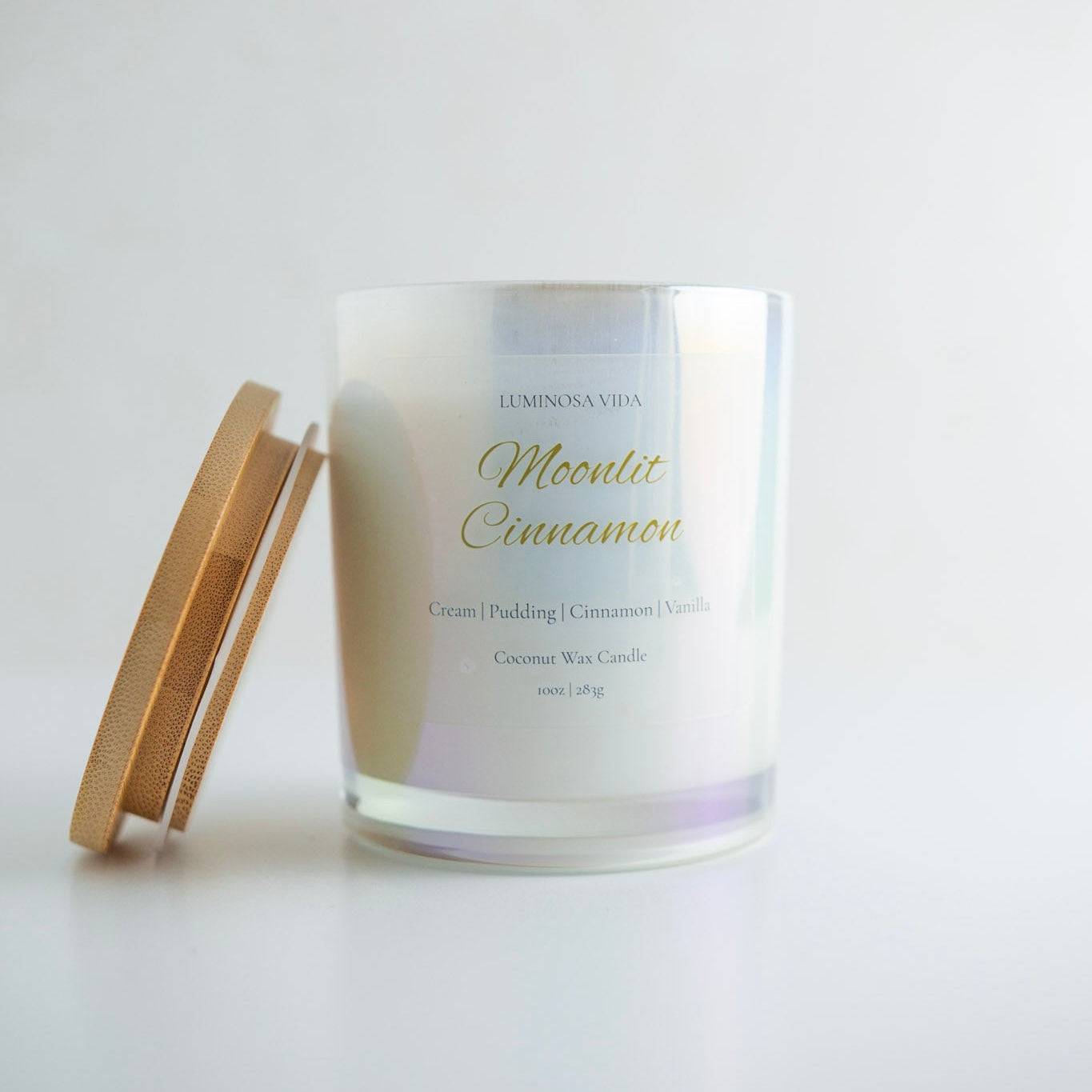 “Luminosa Vida Moonlit Cinnamon candle in an iridescent glass jar with a natural wood lid. Luxury coconut wax candle handcrafted in Austin, Texas with notes of cream, pudding, cinnamon, and vanilla.”
