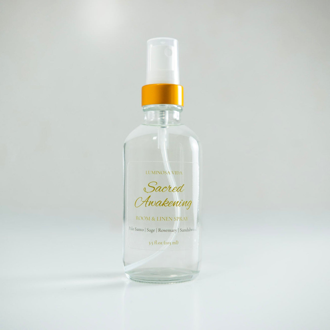 “Sacred Awakening Room + Linen Spray by Luminosa Vida displayed on a white surface with a soft neutral background. A clear glass bottle with a gold cap and refined label showcasing scent notes of Palo Santo, Sage, Rosemary, and Sandalwood — a handcrafted, non-toxic room spray made in Austin, Texas.”