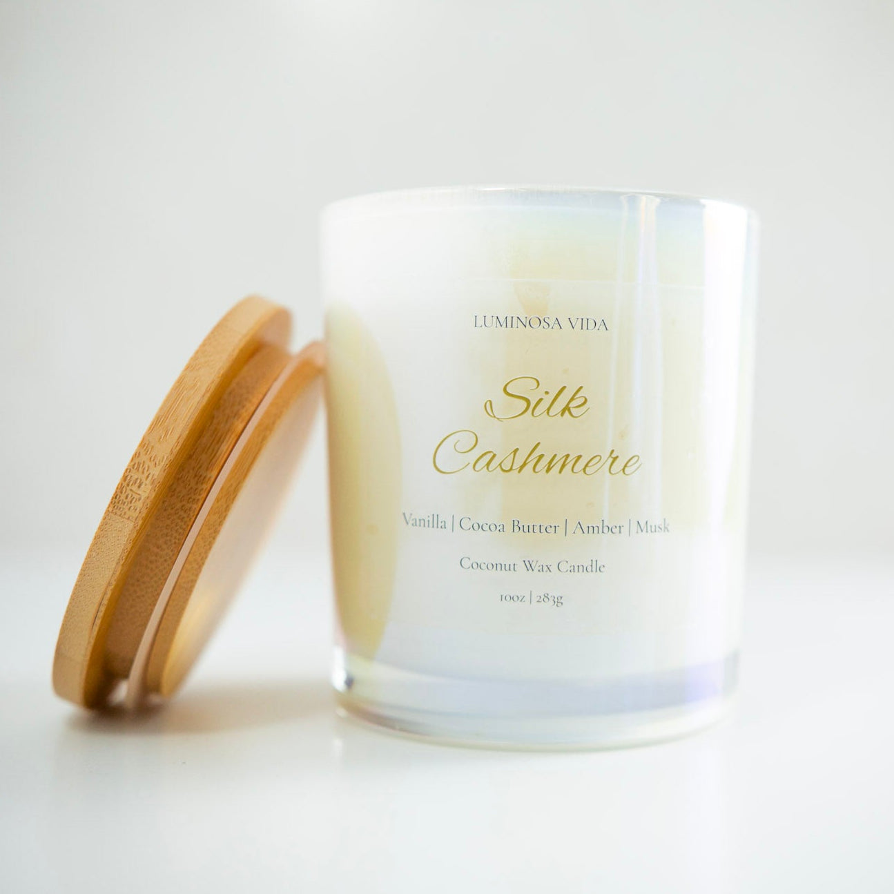 “Luminosa Vida Silk Cashmere candle in an iridescent glass jar with a wooden lid. Luxury coconut wax candle handcrafted in Austin, Texas with notes of vanilla, cocoa butter, amber, and musk — a warm, velvety scent that embodies comfort and elegance.”