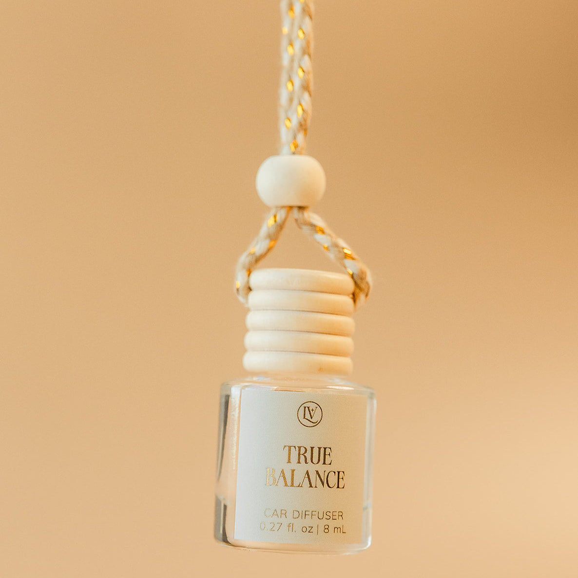 Luminosa Vida True Balance hanging car diffuser with braided cord in a warm neutral lifestyle setting.