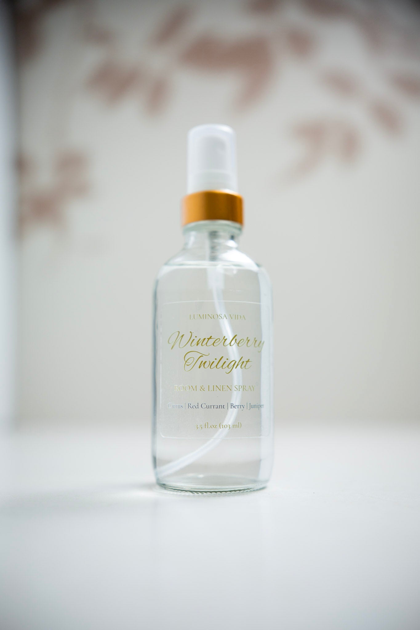 “Winterberry Twilight Room + Linen Spray by Luminosa Vida displayed on a clean white surface with a softly blurred neutral background. A clear glass bottle with a gold cap and elegant label featuring scent notes of Citrus, Red Currant, Berry, and Juniper — a handcrafted, non-toxic home fragrance made in Austin, Texas.”