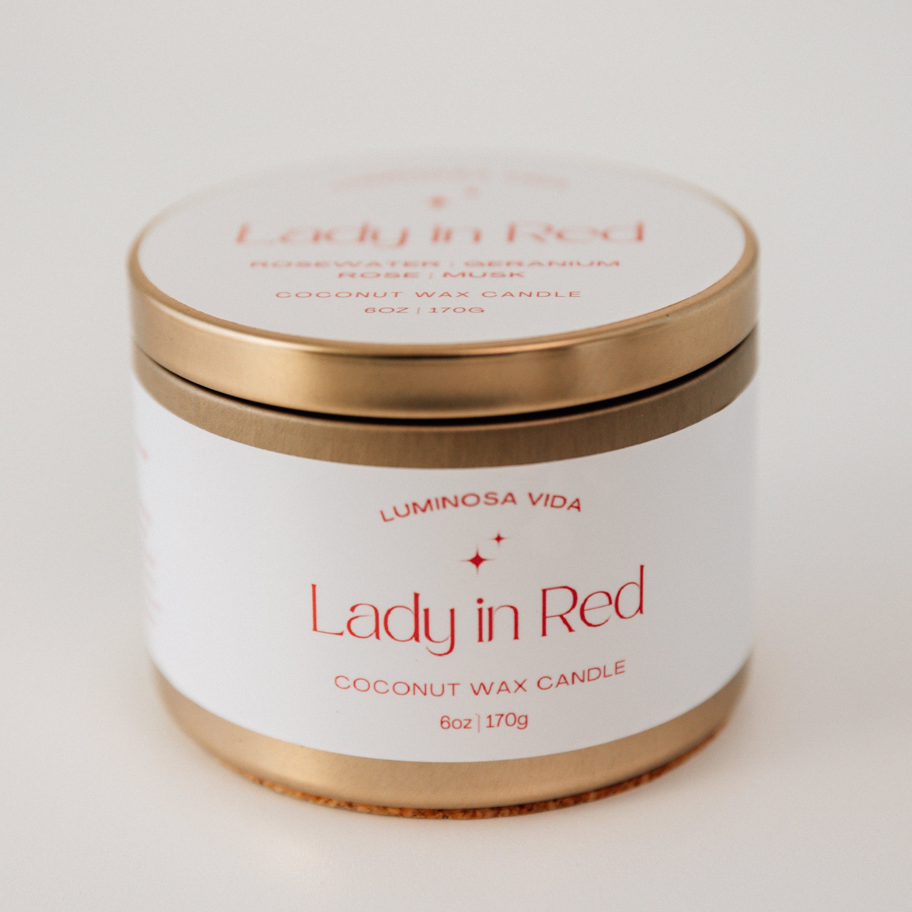 Striking candle labeled 'Lady in Red,' featuring a deep red wax in a sleek container, surrounded by scattered red rose petals and a romantic ambiance. The setup exudes boldness, passion, and elegance.