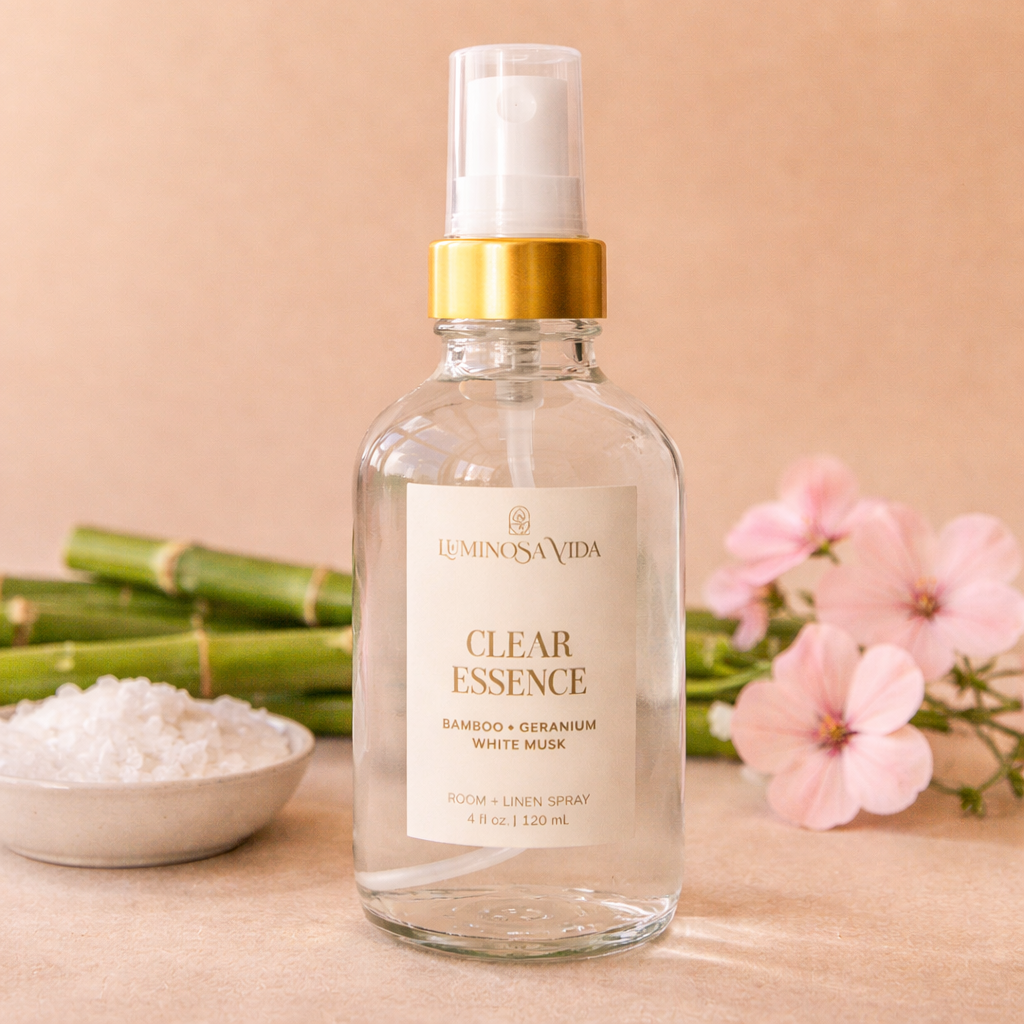Luminosa Vida Clear Essence room and linen spray with bamboo, geranium, and white musk styled with bamboo stems and soft pink flowers.