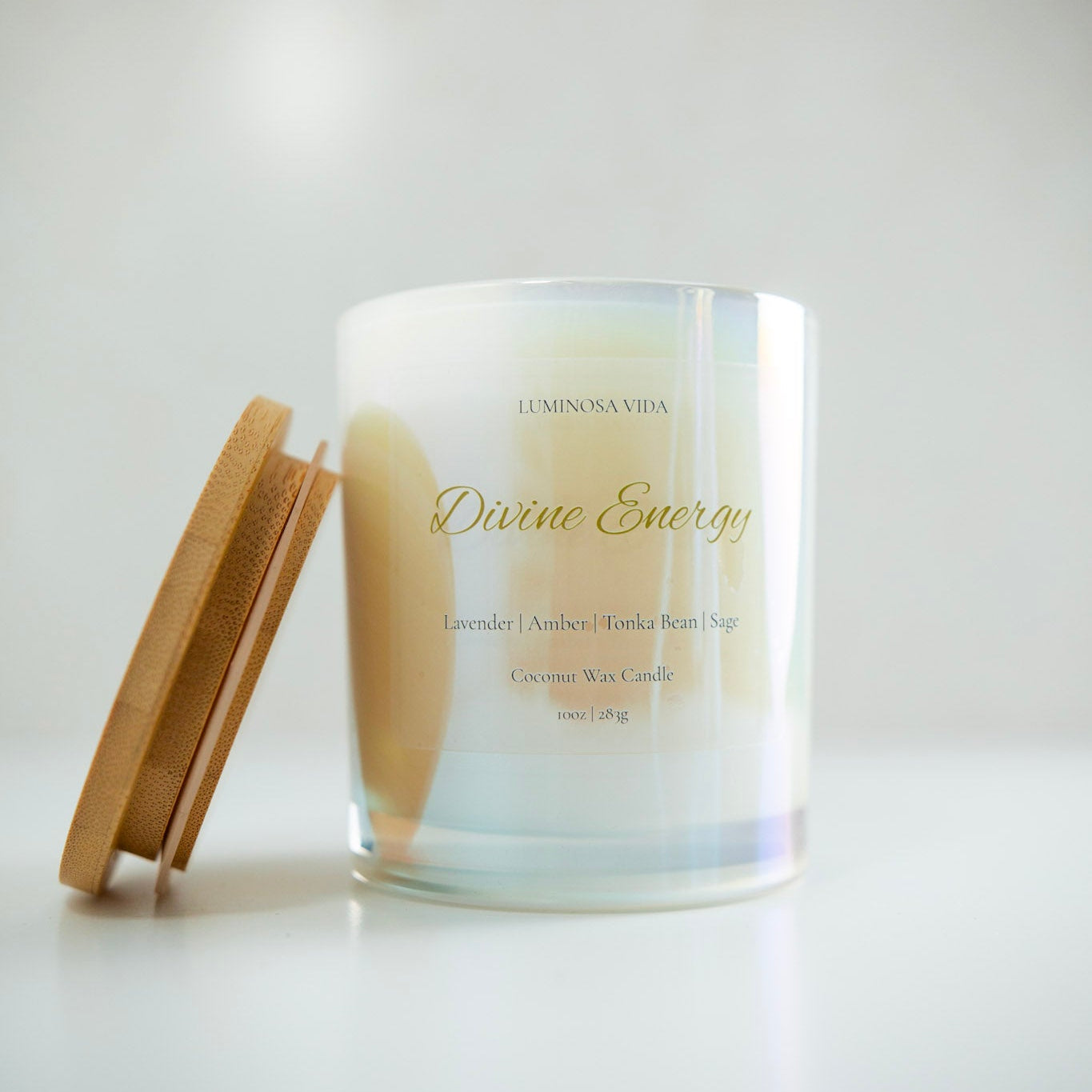 “Luminosa Vida Divine Energy candle in an iridescent glass jar with a wooden lid. Luxury coconut wax candle handcrafted in Austin, Texas with notes of lavender, amber, tonka bean, and sage — a soothing and balanced aromatherapy scent.”