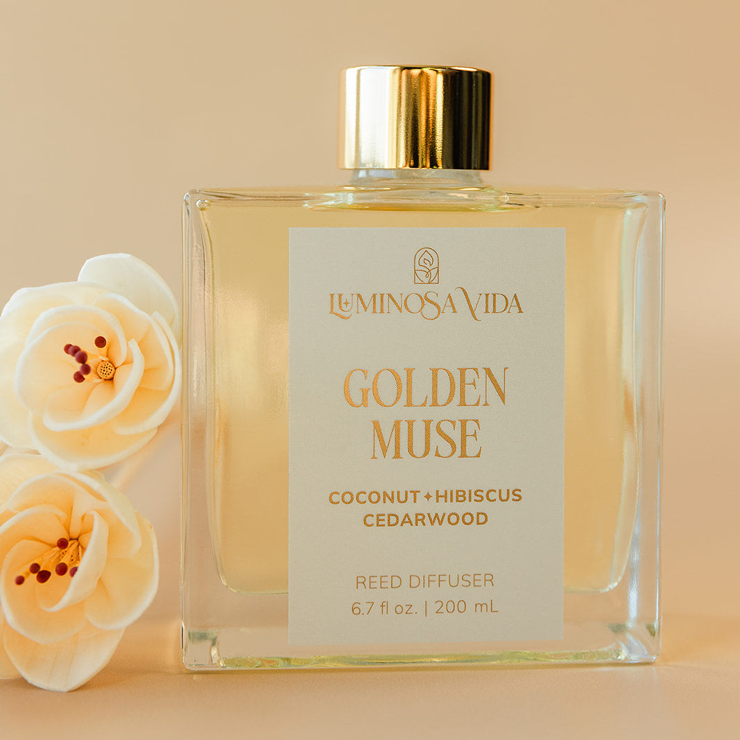 Luminosa Vida Golden Muse reed diffuser with coconut, hibiscus and cedarwood fragrance in a clear glass bottle with gold lid.