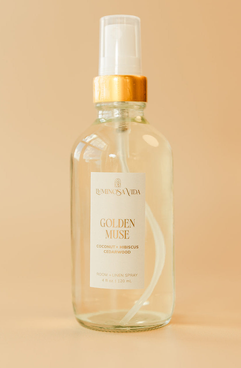 Luminosa Vida Golden Muse room and linen spray with coconut, hibiscus, and cedarwood in a clear glass bottle.