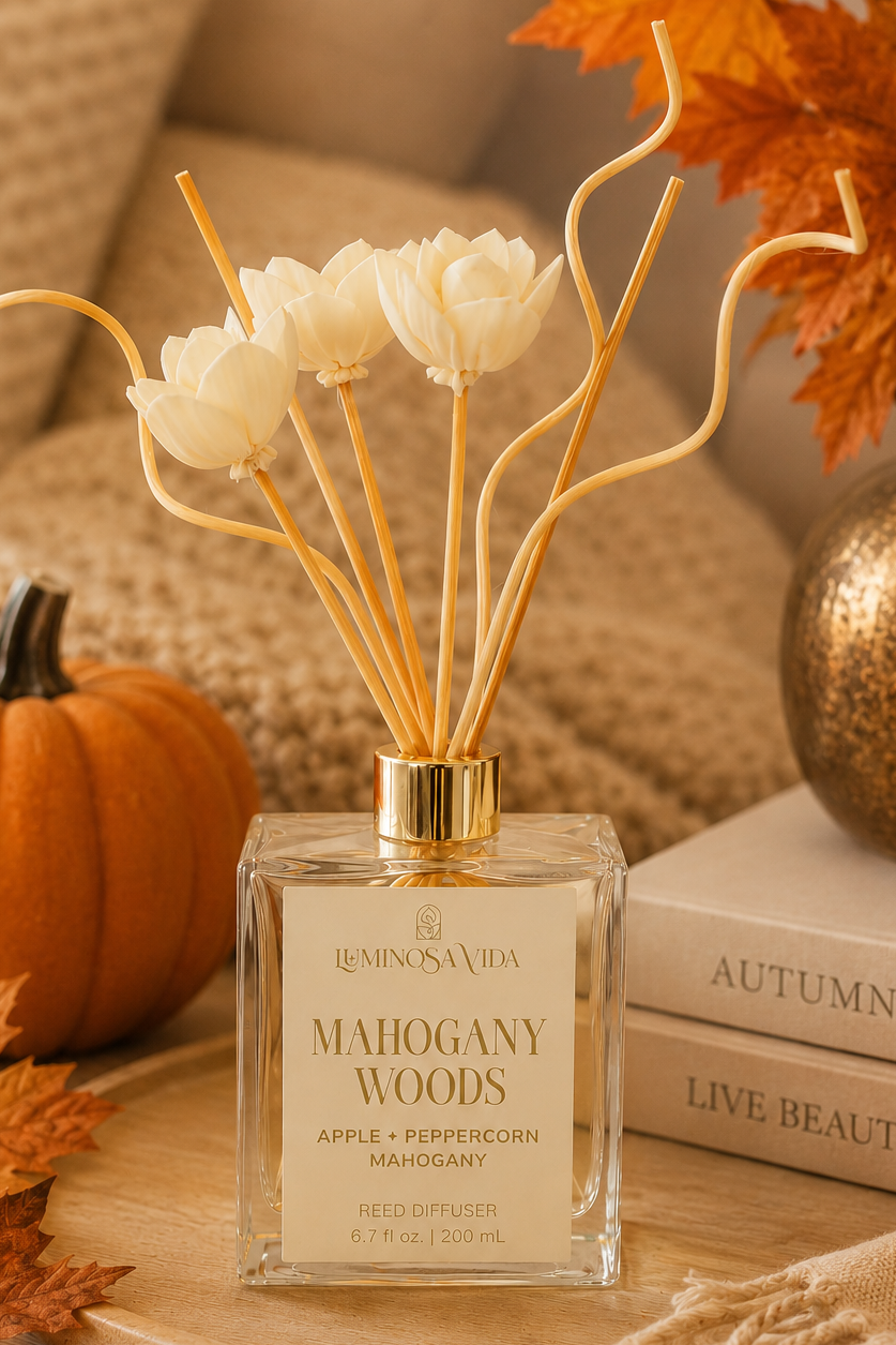 Luminosa Vida Mahogany Woods Reed Diffuser styled in a cozy fall living room with a pumpkin, autumn leaves, soft knit blankets, and warm seasonal décor. Features notes of apple, peppercorn, and mahogany for long-lasting autumn home fragrance.