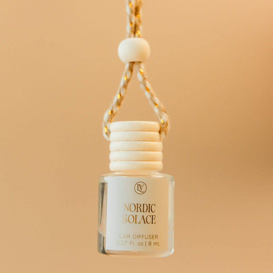 Luminosa Vida Nordic Solace hanging car diffuser with braided cord in a warm neutral lifestyle setting.