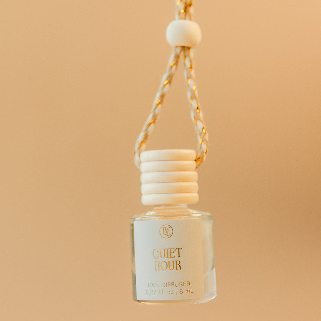 Luminosa Vida Quiet Hour hanging car diffuser with braided cord in a warm neutral lifestyle setting.