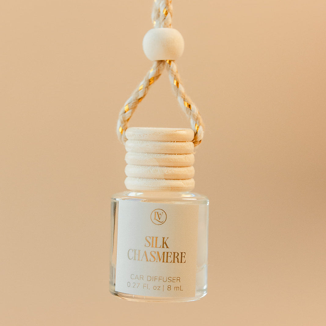 Luminosa Vida Silk Chasmere hanging car diffuser with braided cord in a warm neutral lifestyle setting.
