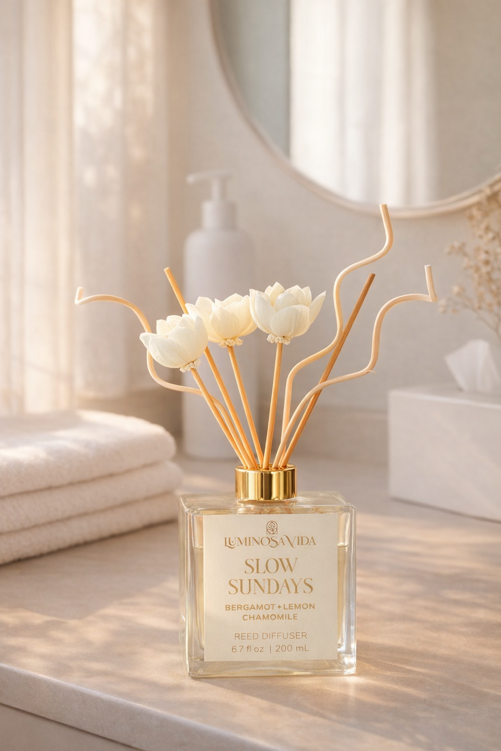 Luxury reed diffuser labeled “Slow Sundays” by Luminosa Vida with bergamot, lemon, and chamomile fragrance in a glass bottle with gold cap and sola flower reeds in soft natural morning light.