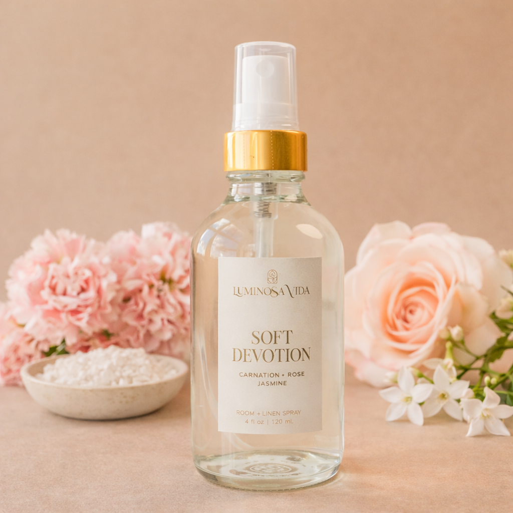 Luminosa Vida Soft Devotion room and linen spray with carnation, rose, and jasmine styled with pink flowers and mineral salt on a soft neutral background.