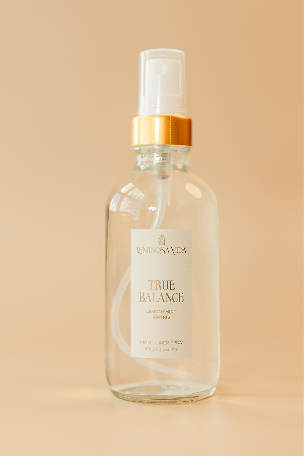 Luminosa Vida True Balance room and linen spray with lemon, mint, and amyris in a clear glass bottle with gold collar on a neutral background.