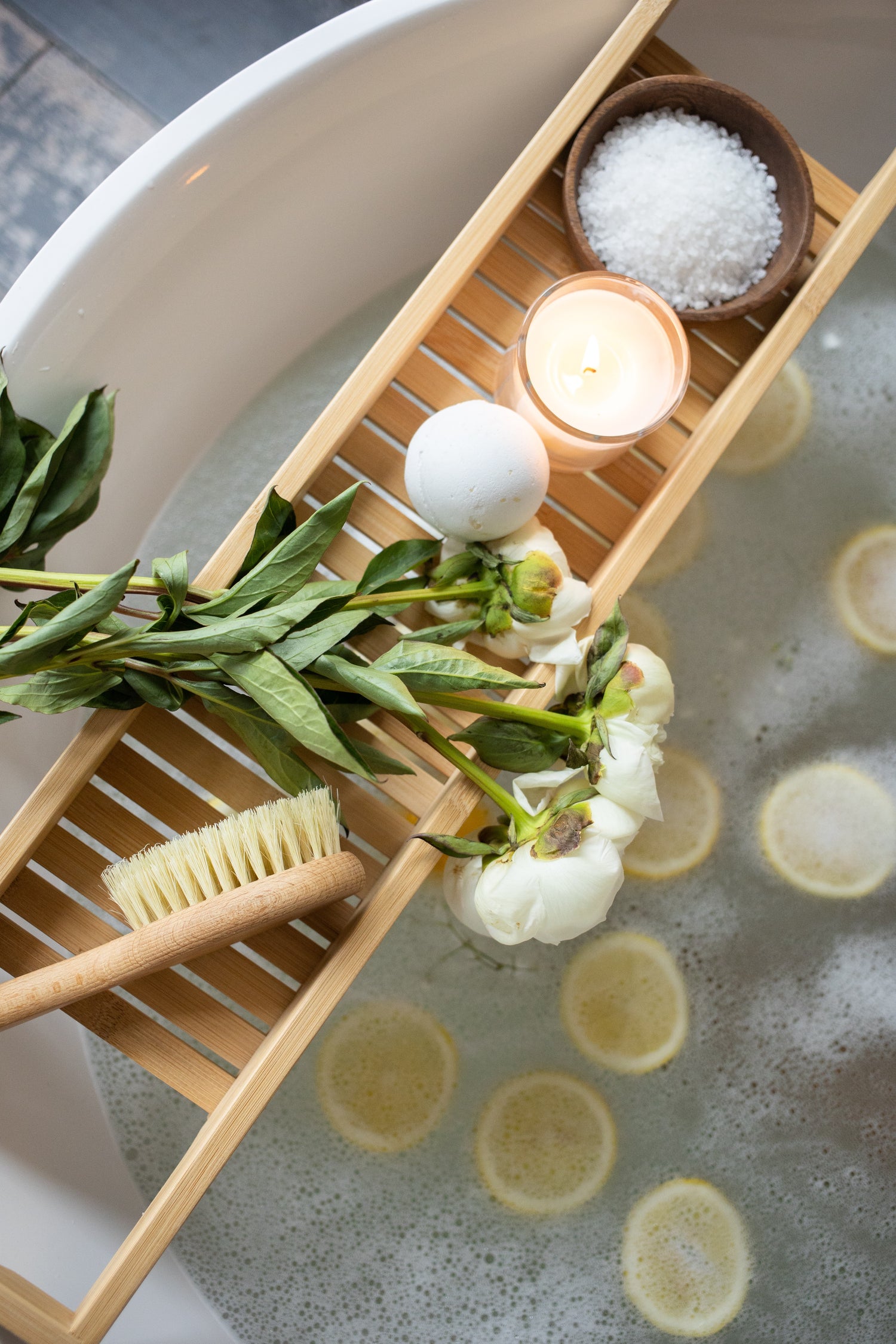 candles, bath salts, flowers and brush in bath tub with lemons for relaxing bath, self care, bath, relaxation