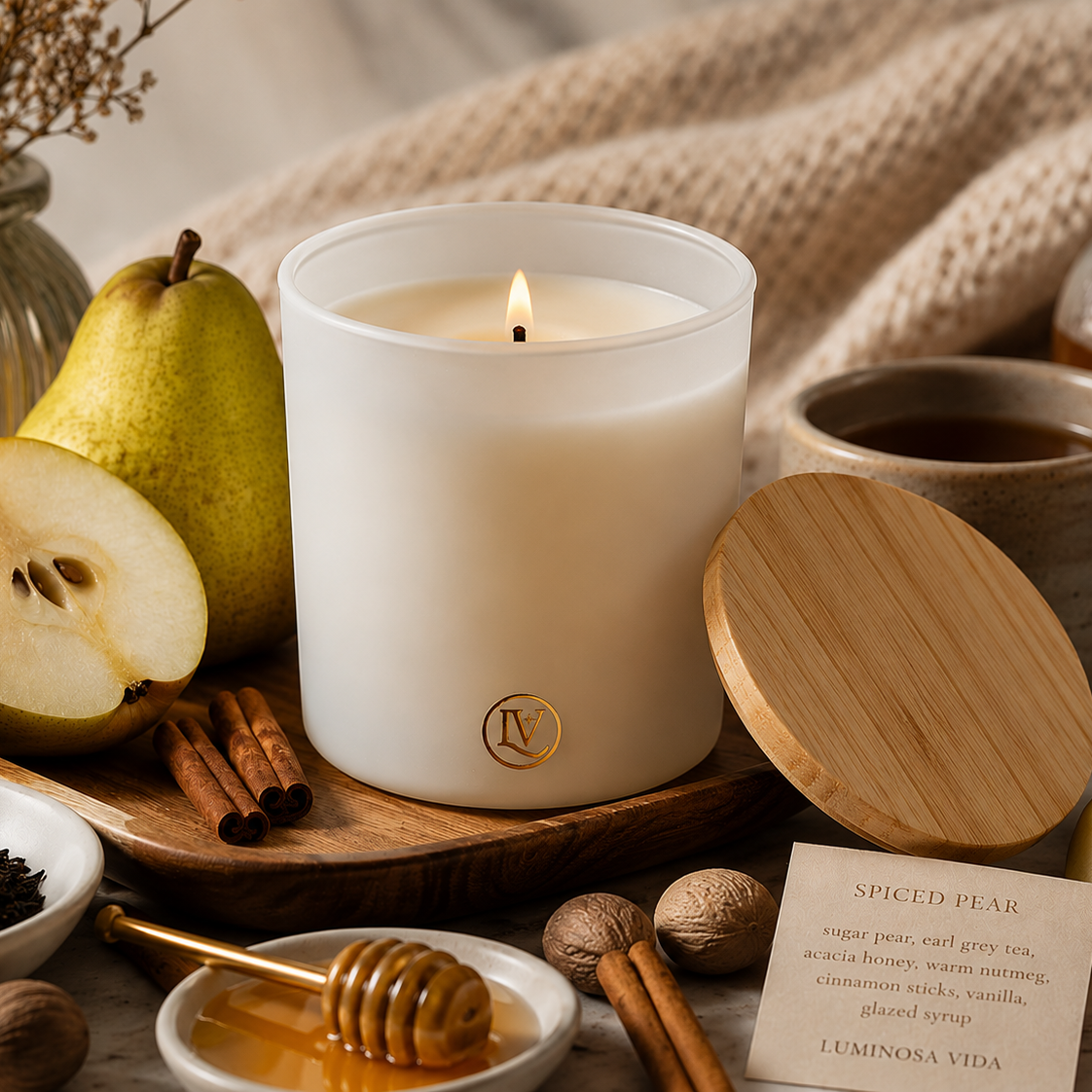 Lit Spiced Pear luxury coconut wax candle by Luminosa Vida with the lid removed, styled with fresh pears, Earl Grey tea, honey, cinnamon sticks and cozy fall décor.